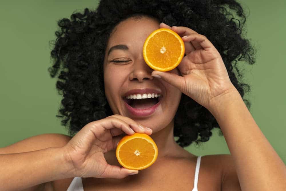 Mujer sonriente con dos mitades de naranja, fuente de vitamina C